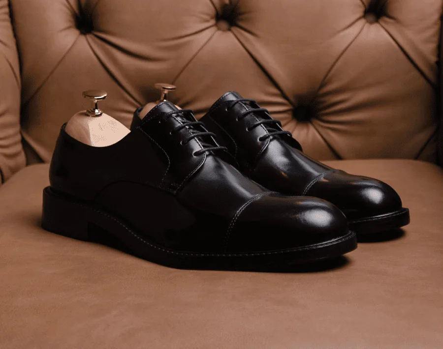 Par de sapatos pretos sobre um sofá de couro capitonê.